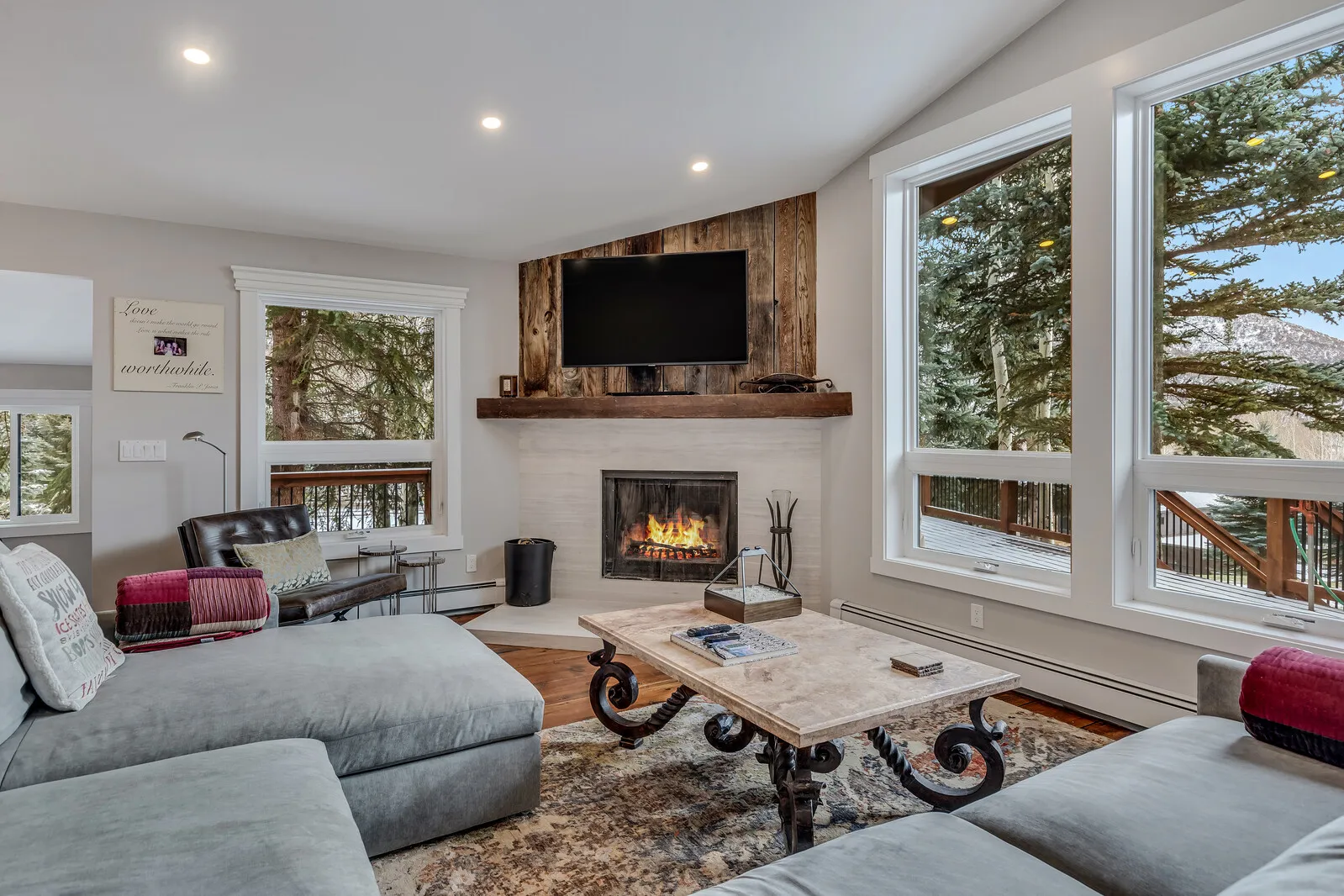 The great room: sectional sofa, fireplace and tall windows to the trees